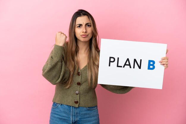 Jonge blanke vrouw geïsoleerd op roze achtergrond met een bordje met het bericht PLAN B en boos