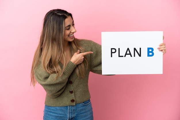 Jonge blanke vrouw geïsoleerd op roze achtergrond met een bordje met het bericht plan b