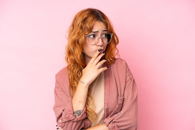 Jonge blanke vrouw geïsoleerd op roze achtergrond Met een bril en twijfels