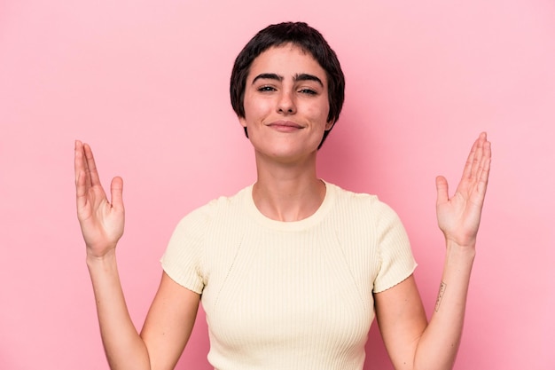 Foto jonge blanke vrouw geïsoleerd op roze achtergrond met iets kleins met wijsvingers glimlachend en zelfverzekerd