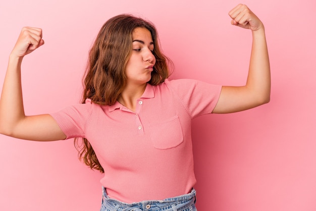 Jonge blanke vrouw geïsoleerd op roze achtergrond met krachtgebaar met armen, symbool van vrouwelijke kracht