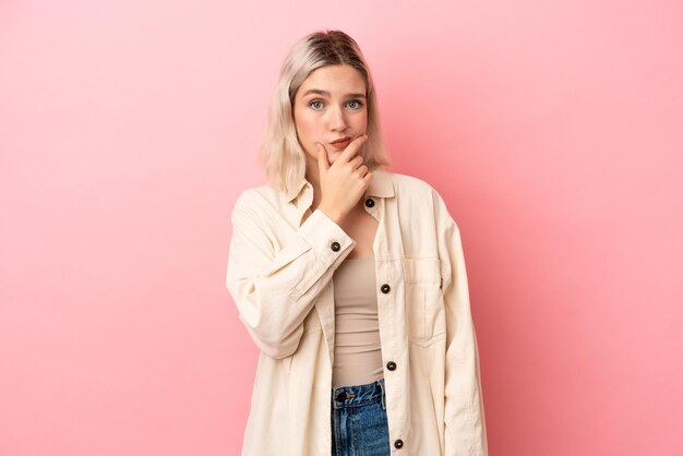 Jonge blanke vrouw geïsoleerd op roze achtergrond met twijfels