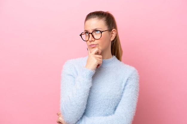 Jonge blanke vrouw geïsoleerd op roze achtergrond met twijfels