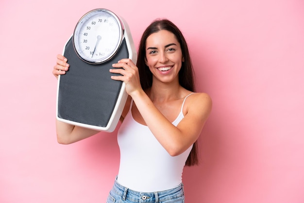 Jonge blanke vrouw geïsoleerd op roze achtergrond met weegmachine