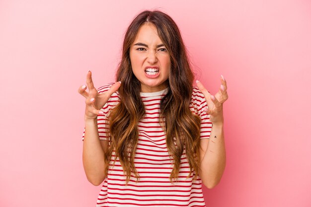 Jonge blanke vrouw geïsoleerd op roze achtergrond schreeuwen van woede.