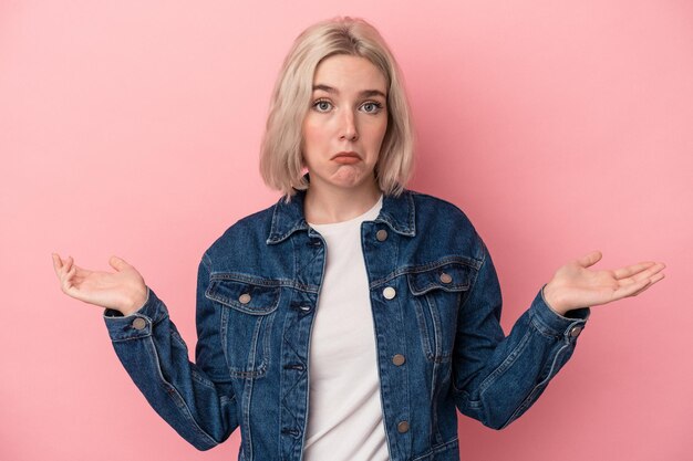 Jonge blanke vrouw geïsoleerd op roze achtergrond twijfelen en schouders ophalen in ondervraging gebaar.