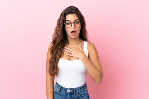 Jonge blanke vrouw geïsoleerd op roze achtergrond verrast en geschokt terwijl ze naar rechts kijkt