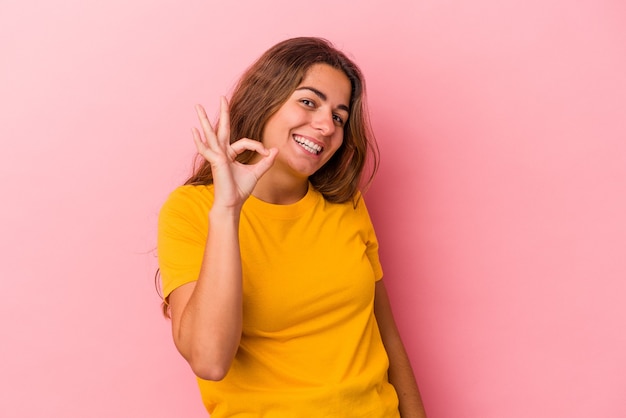 Jonge blanke vrouw geïsoleerd op roze achtergrond vrolijk en zelfverzekerd weergegeven: ok gebaar.