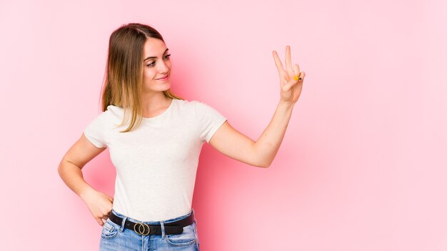 Jonge blanke vrouw geïsoleerd op roze achtergrond vrolijk en zorgeloos met een vredessymbool met vingers.