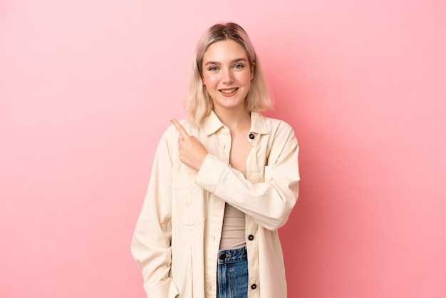 Jonge blanke vrouw geïsoleerd op roze achtergrond wijzend naar de zijkant om een product te presenteren