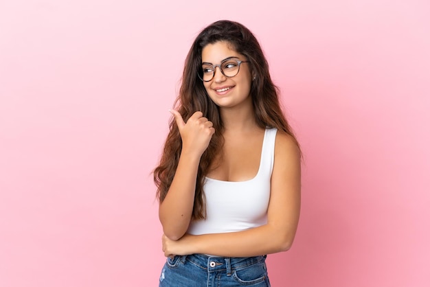 Jonge blanke vrouw geïsoleerd op roze achtergrond wijzend naar de zijkant om een product te presenteren