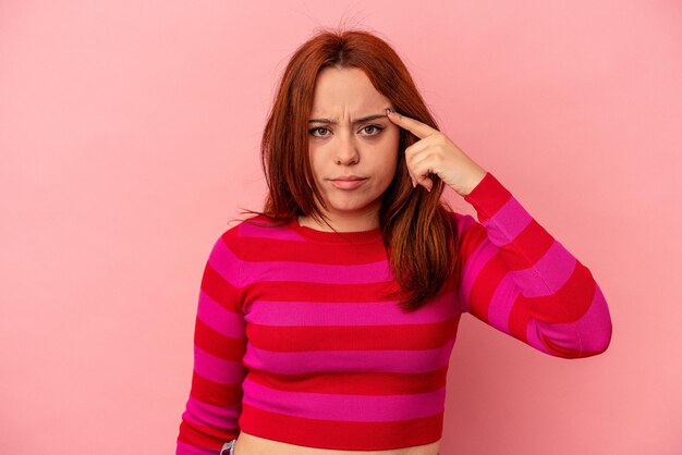 Jonge blanke vrouw geïsoleerd op roze achtergrond wijzende tempel met vinger, denken, gericht op een taak.