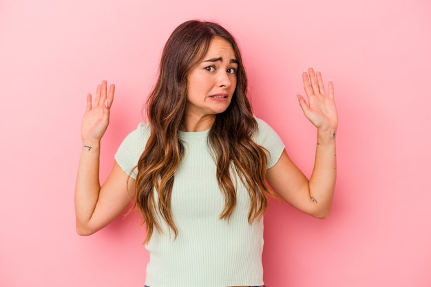 Jonge blanke vrouw geïsoleerd op roze achtergrond wordt geschokt door een dreigend gevaar