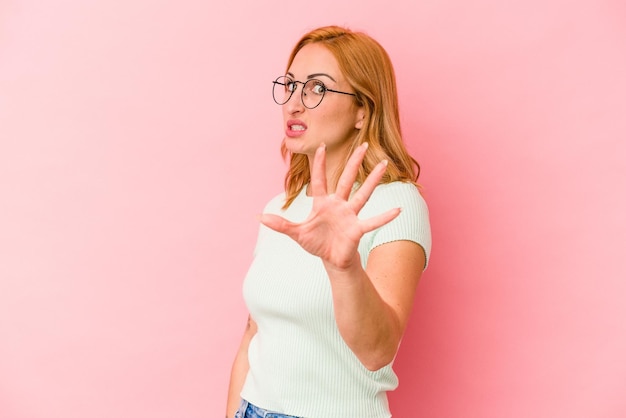 Jonge blanke vrouw geïsoleerd op roze achtergrond wordt geschokt door een dreigend gevaar