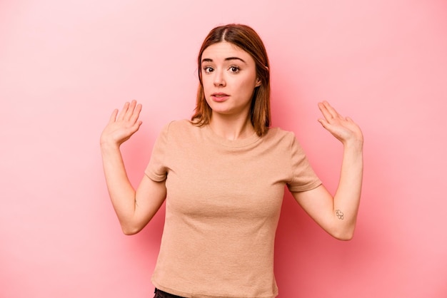 Jonge blanke vrouw geïsoleerd op roze achtergrond wordt geschokt door een dreigend gevaar