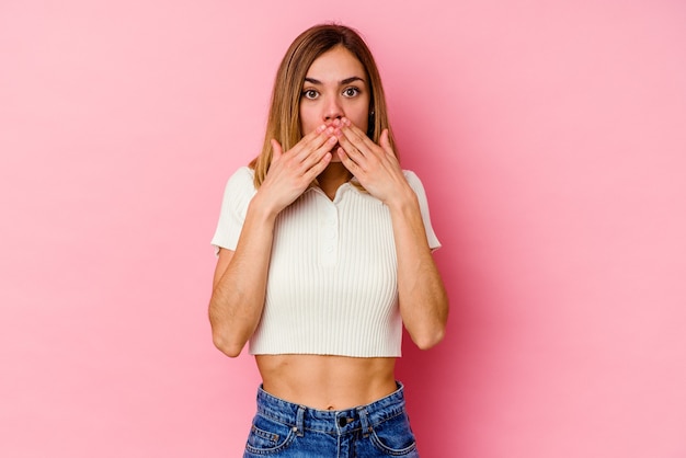 Jonge blanke vrouw geïsoleerd op roze geschokt, mond bedekt met handen, angstig om iets nieuws te ontdekken.