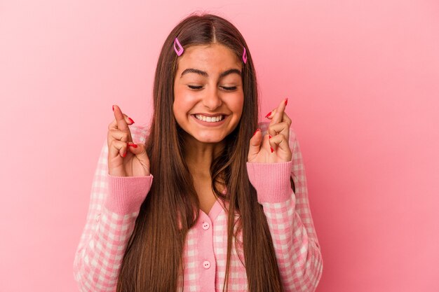 Jonge blanke vrouw geïsoleerd op roze muur die vingers kruist om geluk te hebben
