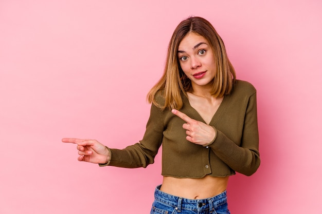 Jonge blanke vrouw geïsoleerd op roze muur geschokt wijzend met wijsvingers naar een kopie ruimte