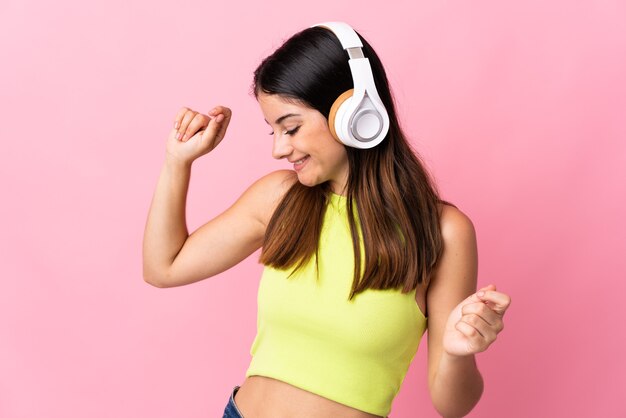 Jonge blanke vrouw geïsoleerd op roze muur luisteren muziek en dansen