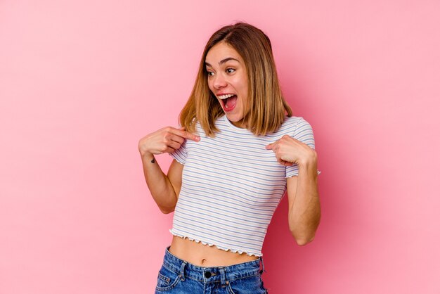 Jonge blanke vrouw geïsoleerd op roze muur verrast wijzend met vinger, breed glimlachend.