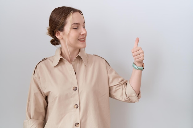 Jonge blanke vrouw, gekleed in casual shirt, trots kijkend, glimlachend met duim omhoog gebaar naar de zijkant