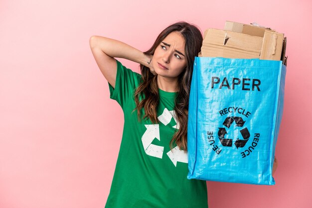 Jonge blanke vrouw gerecycled papier geïsoleerd op een roze achtergrond die achterhoofd aanraakt en een keuze maakt