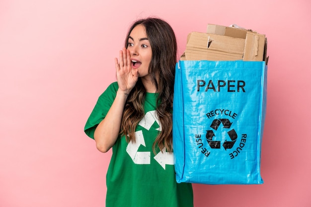 Jonge blanke vrouw gerecycled papier geïsoleerd op roze achtergrond schreeuwen en houden palm in de buurt van geopende mond