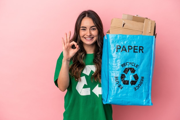 Jonge blanke vrouw gerecycled papier geïsoleerd op roze achtergrond vrolijk en zelfverzekerd weergegeven: ok gebaar.