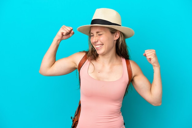 Jonge blanke vrouw in zomervakantie geïsoleerd op blauwe achtergrond die een overwinning viert