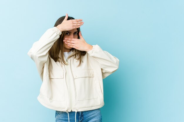 Jonge blanke vrouw knippert met haar vingers naar de camera, beschaamd bedekkend gezicht.