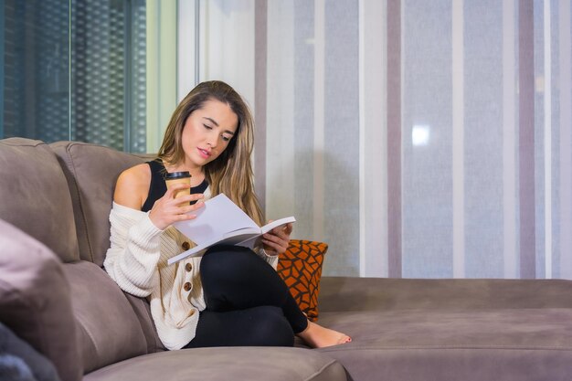 Jonge blanke vrouw leest een boek op de bank in haar woonkamer