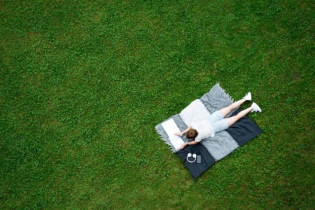 Jonge blanke vrouw liggend op de deken op groen gazon en het lezen van een boek