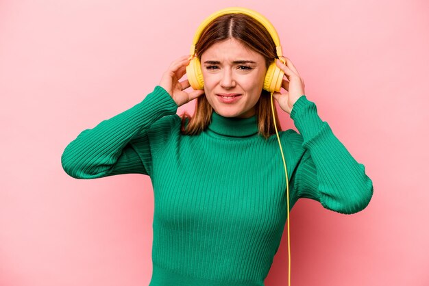 Jonge blanke vrouw luisteren naar muziek geïsoleerd op roze achtergrond die oren bedekt met handen