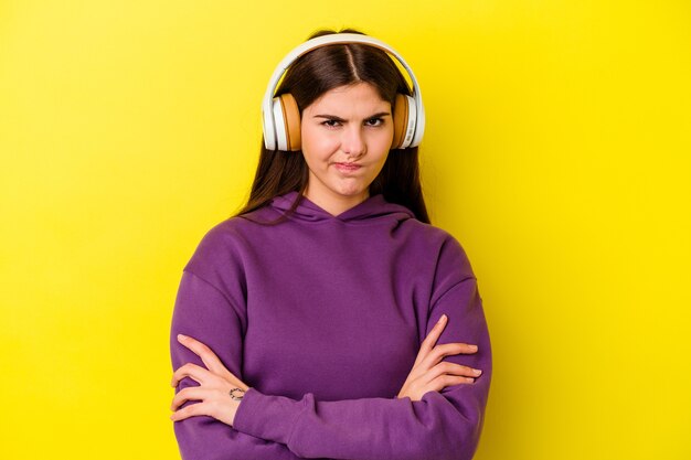 Jonge blanke vrouw luisteren naar muziek met koptelefoon geïsoleerd op roze achtergrond fronsend gezicht in ongenoegen, houdt armen gevouwen.