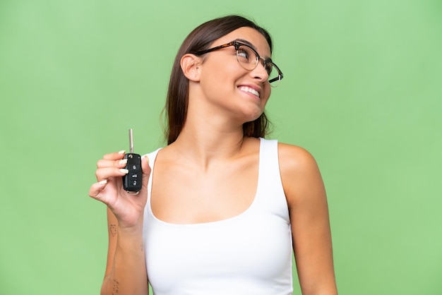 Jonge blanke vrouw met autosleutels geïsoleerd op groene chroma achtergrond achtergrond opzoeken terwijl glimlachen