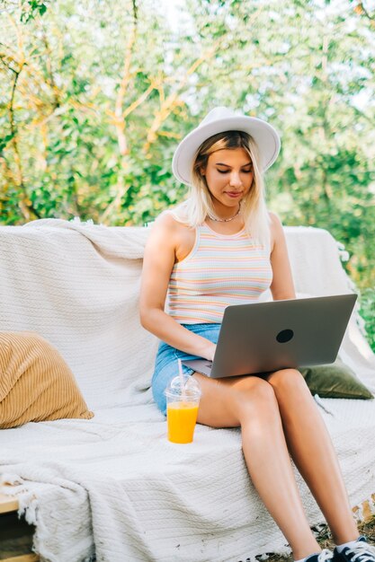 Jonge blanke vrouw met behulp van laptopcomputer buiten, zittend op een bankje in de achtertuin in zomerdag.