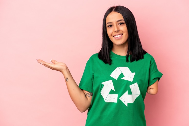 Foto jonge blanke vrouw met één arm gerecycled afval geïsoleerd op roze achtergrond met een kopie ruimte op een palm en met een andere hand op de taille.