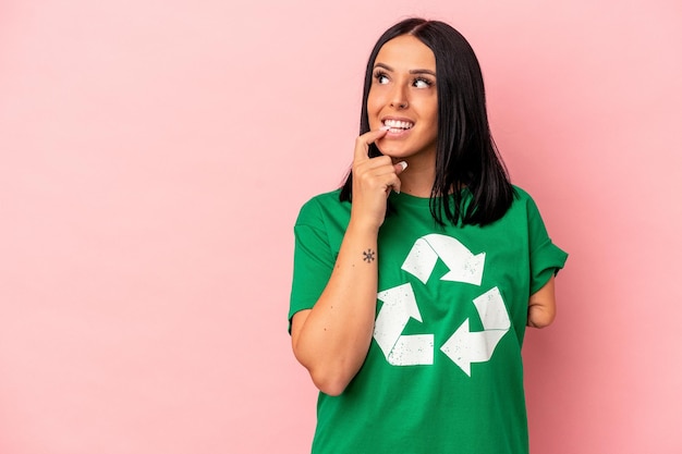 Jonge blanke vrouw met één arm gerecycled afval geïsoleerd op roze achtergrond ontspannen denken over iets kijken naar een kopie ruimte.