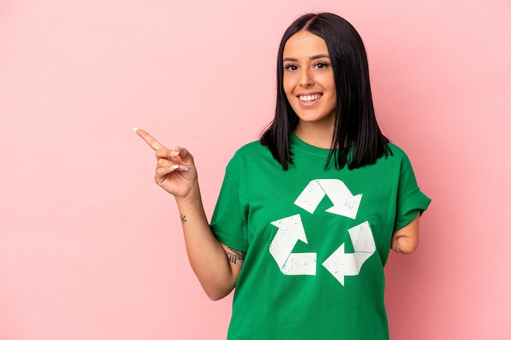 Foto jonge blanke vrouw met één arm gerecycleerd afval geïsoleerd op roze achtergrond glimlachend en opzij wijzend, iets tonend op lege ruimte.