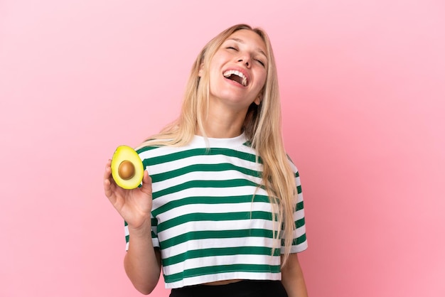 Jonge blanke vrouw met een avocado geïsoleerd op roze achtergrond lachen