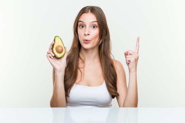 Jonge blanke vrouw met een avocado met een geweldig idee