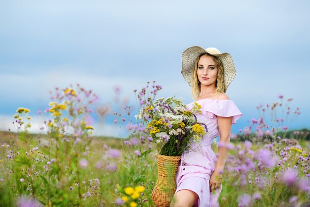 Jonge blanke vrouw met een boeket van wilde bloemen. Meisje in een strohoed poseren in de natuur.