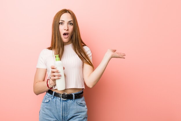 Jonge blanke vrouw met een crème fles onder de indruk kopie ruimte op palm te houden.