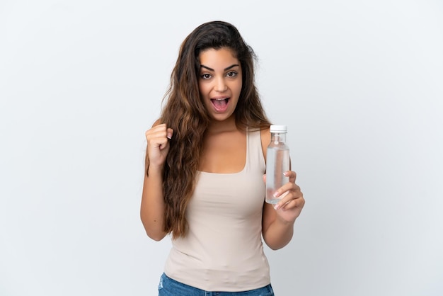 Jonge blanke vrouw met een fles water geïsoleerd op een witte achtergrond die een overwinning viert in winnaarspositie