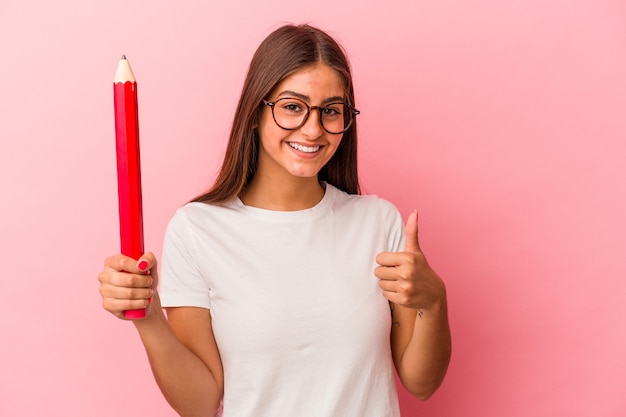 Jonge blanke vrouw met een groot potlood geïsoleerd op een roze muur glimlachend en duim omhoog