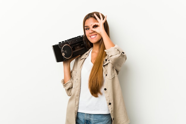 Jonge blanke vrouw met een guetto blaster opgewonden houden ok gebaar op oog.