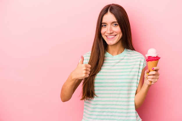 Jonge blanke vrouw met een ijsje geïsoleerd op een roze achtergrond glimlachend en duim omhoog