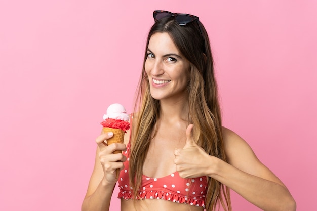 Jonge blanke vrouw met een ijsje geïsoleerd op roze achtergrond met duimen omhoog omdat er iets goeds is gebeurd