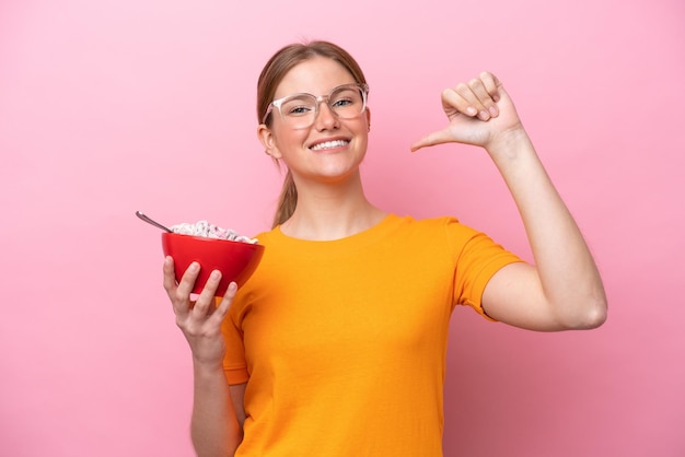 Jonge blanke vrouw met een kom ontbijtgranen geïsoleerd op roze achtergrond trots en zelfvoldaan