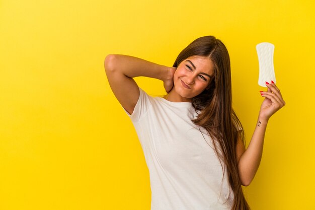 Jonge blanke vrouw met een kompres geïsoleerd op een gele muur die de achterkant van het hoofd aanraakt, denkt en een keuze maakt.